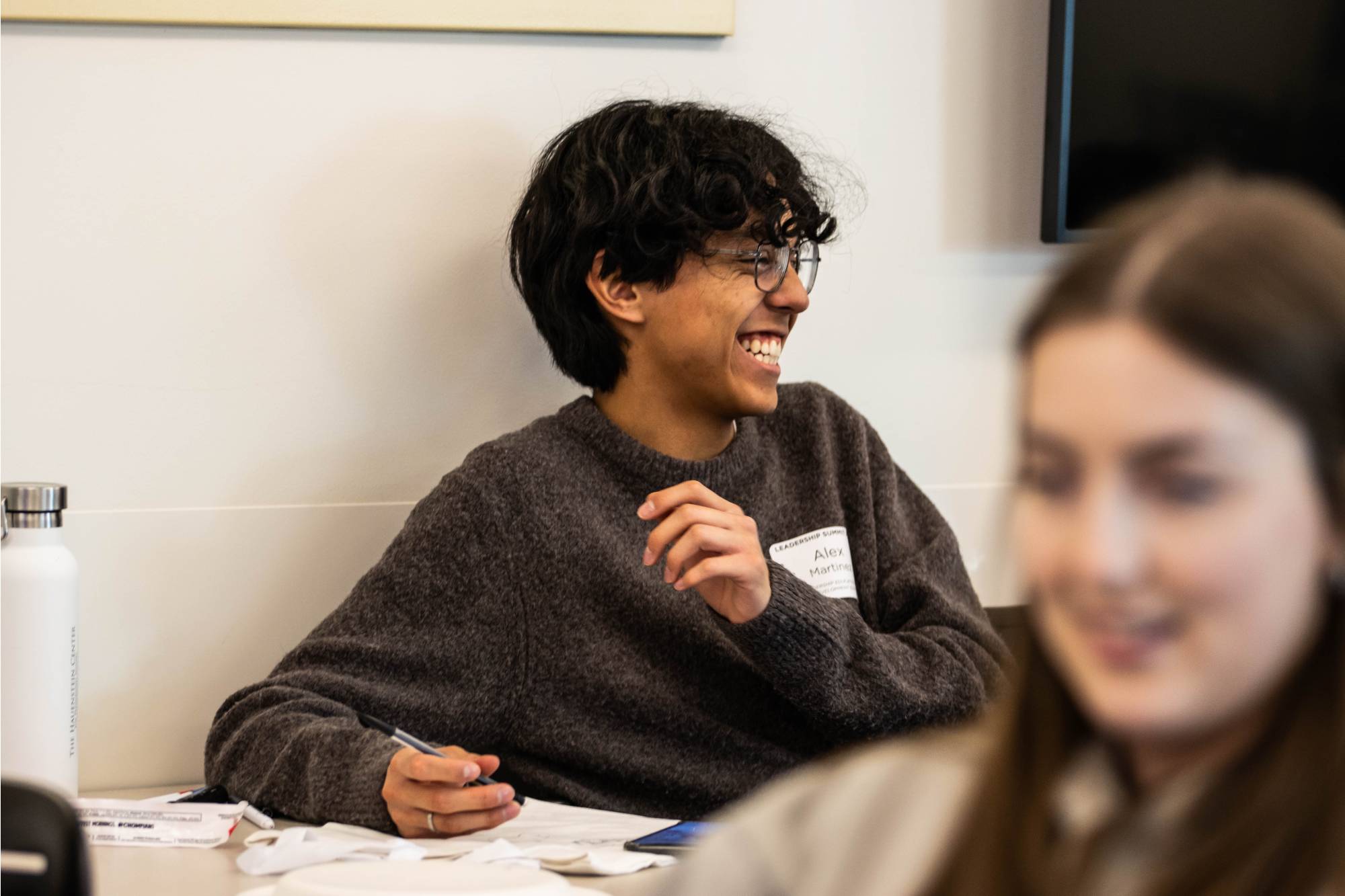 Student smiling and sitting at a table working on a project
